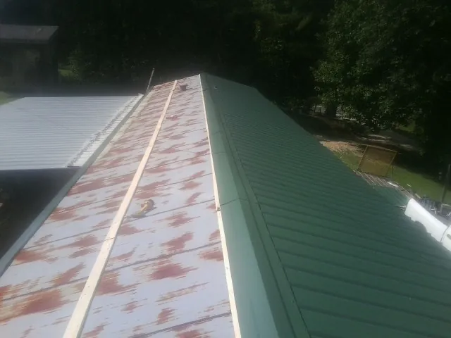 Old rusted panels beside newly installed green metal roofing — Wind Damage Roof Repair by Roofing Brothers in Creston