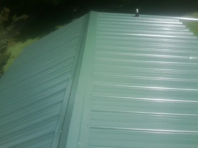 New green metal panels meeting at the ridge of a roof — Flat Roof Repair work by our crew in Creston